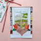 Calendar 2026 with a window view and bookshelf design, tied with a ribbon on a pink background.