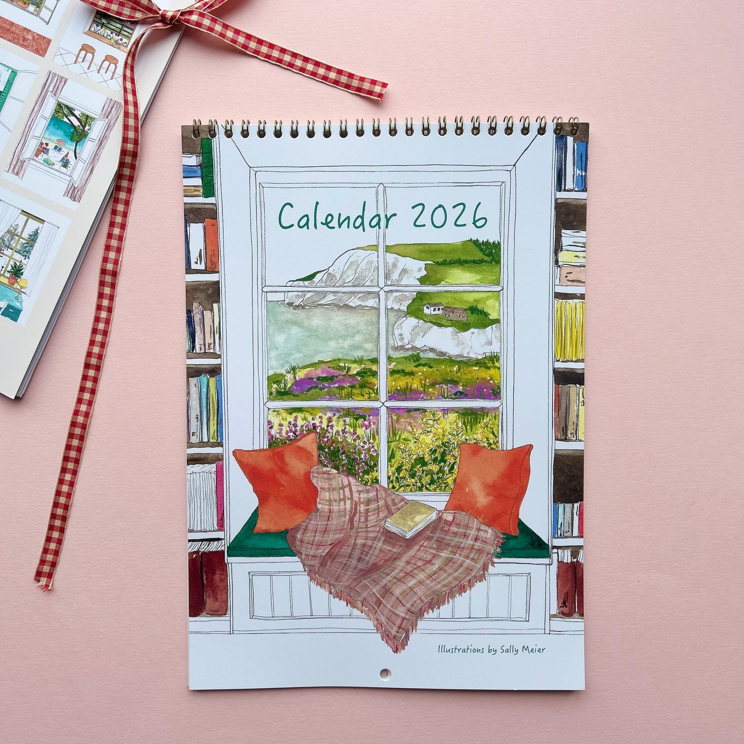 Calendar 2026 with a window view and bookshelf design, tied with a ribbon on a pink background.